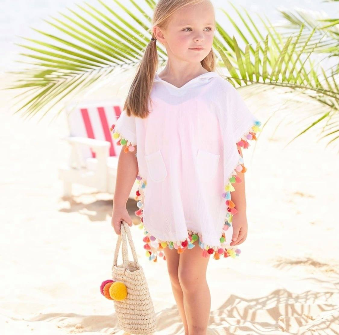 Girl in white pom trim beach coverup holding a woven bag