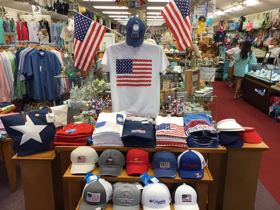 Patriotic South Padre Island tee and cap table with American flags, striped shirts, visors and tote bag