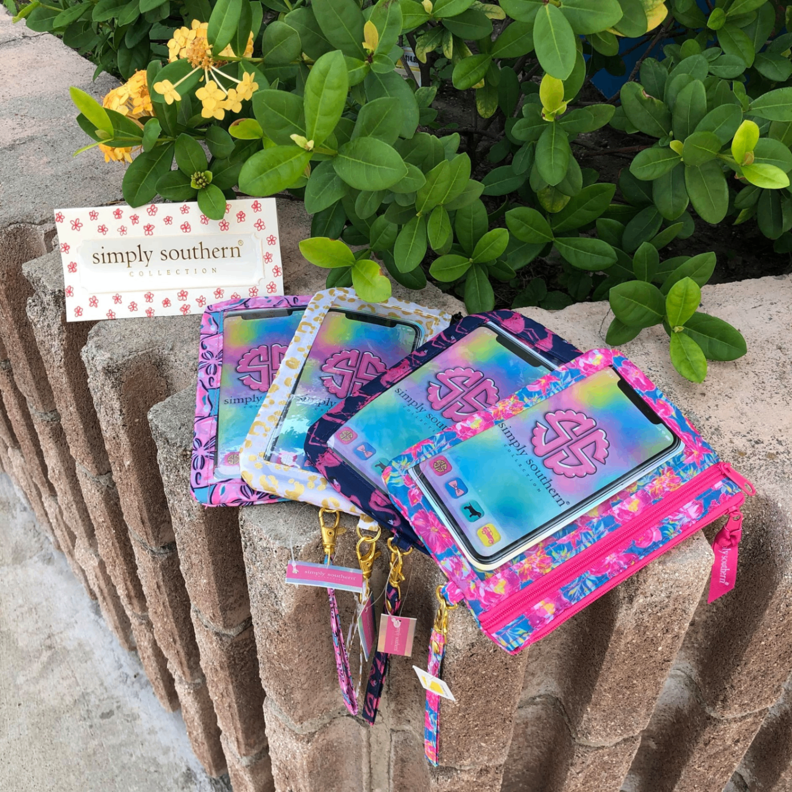 Simply Southern phone wristlets in tropical pink, navy and floral prints on a stone garden ledge