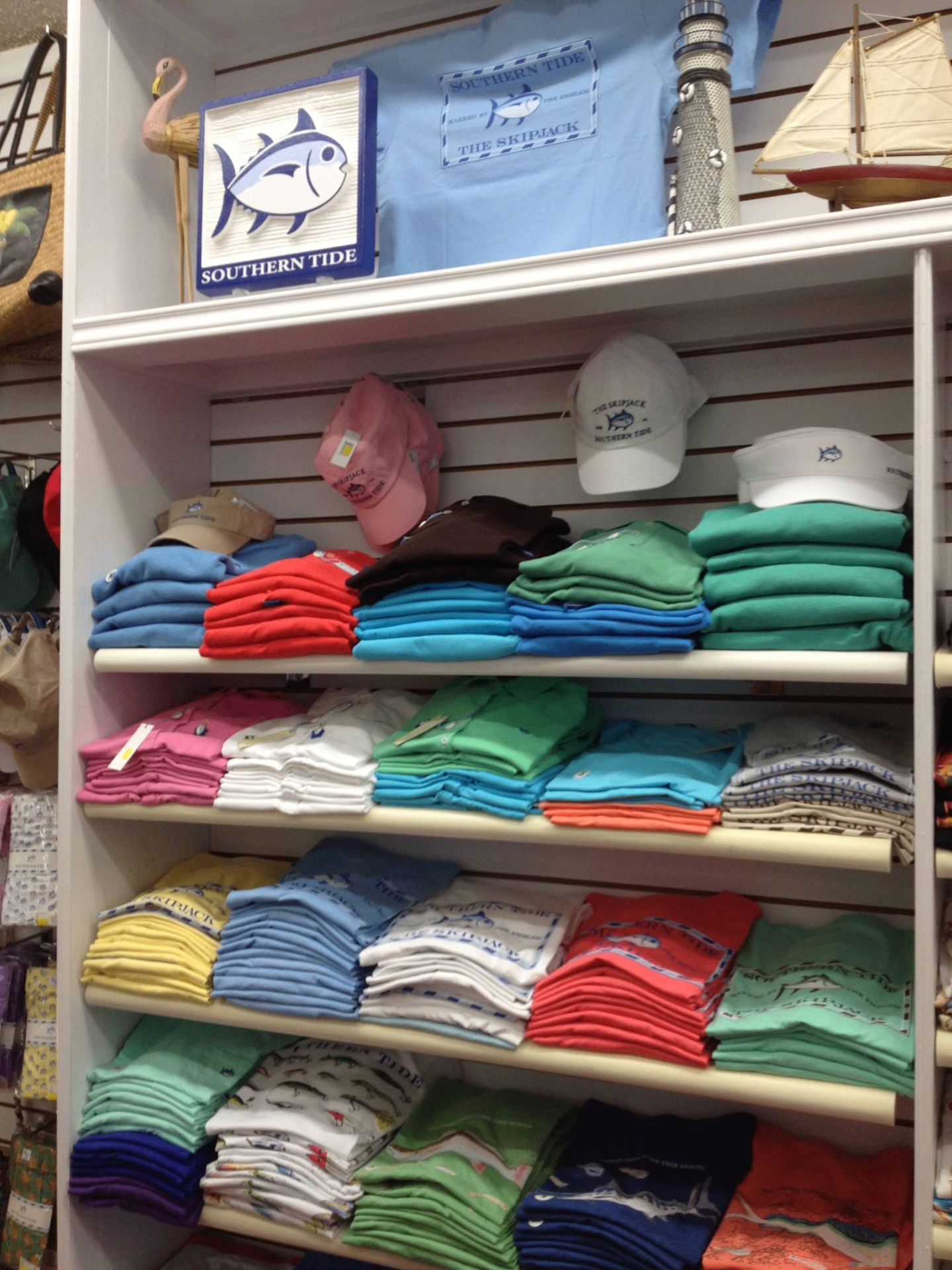 Southern Tide shelf display with folded pastel tees, caps, visor and Skipjack sign inside the boutique